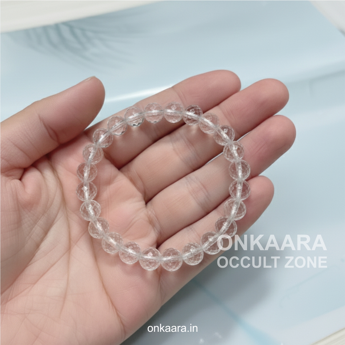 Clear Quartz crystal bracelet with round faceted beads placed on a white stone background.